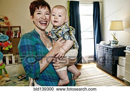 Stock Image - Caucasian mother holding baby in bedroom. Fotosearch