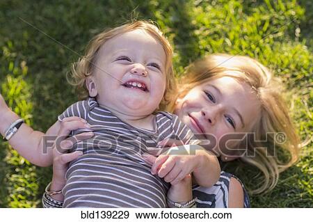 Stock Photo - Caucasian sister holding baby brother in grass. Fotosearch