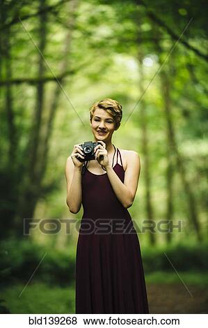 Caucasian woman holding camera in forest View Large Photo Image Stock Photo - Caucasian woman holding camera in forest. Fotosearch