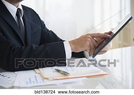 Picture - Close up of mixed race businessman using digital tablet at office desk. Fotosearch