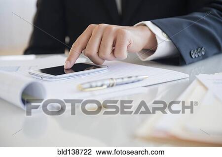 Stock Image - Close up of mixed race businessman using cell phone at desk. Fotosearch