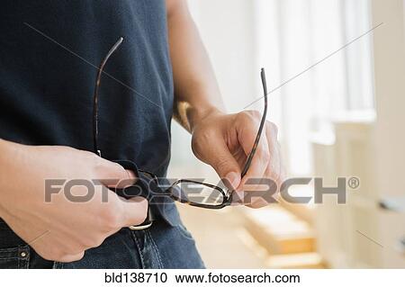 Stock Image - Close up of mixed race man cleaning eyeglasses with shirt. Fotosearch