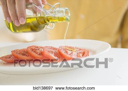 Stock Photo - Close up of mixed race man pouring oil on tomatoes. Fotosearch
