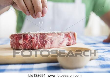 Picture - Close up of mixed race man sprinkling salt on steak. Fotosearch