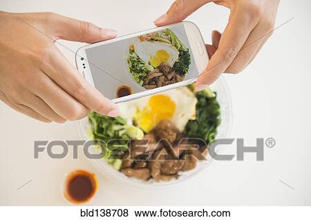 Stock Photo - Close up of mixed race man photographing food with cell phone. Fotosearch