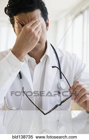 Stock Photography - Close up of upset mixed race doctor rubbing his forehead. Fotosearch