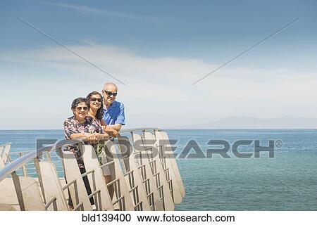 Stock Image - Family smiling together at waterfront railing. Fotosearch