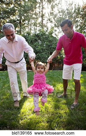 Stock Photography - Father and grandfather helping daughter walk in backyard. Fotosearch