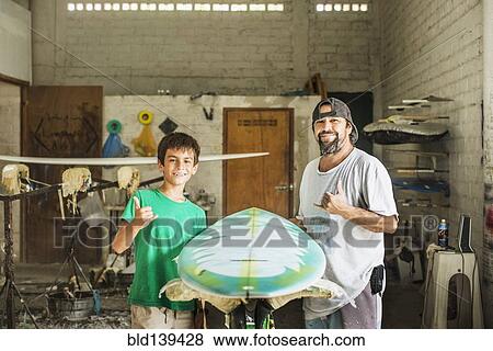Father and son gesturing hang ten in surfboard workshop View Large Photo Image Stock Photo - Father and son gesturing hang ten in surfboard workshop. Fotosearch