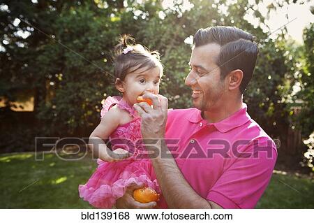 Stock Photo - Father feeding daughter orange outdoors. Fotosearch