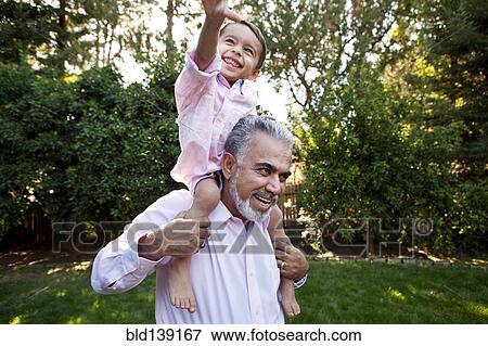 Stock Photo - Grandfather carrying grandson on shoulders in backyard. Fotosearch