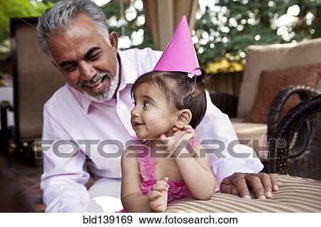Grandfather sitting with granddaughter at birthday party View Large Photo Image Stock Photo - Grandfather sitting with granddaughter at birthday party. Fotosearch