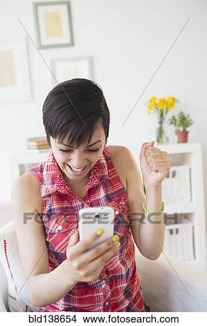 Picture - Happy mixed race woman cheering with cell phone. Fotosearch