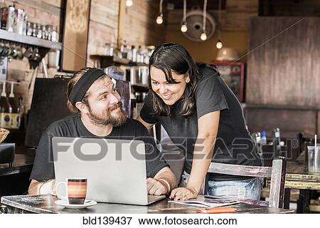 Stock Photo - Hispanic couple using laptop in coffee shop. Fotosearch