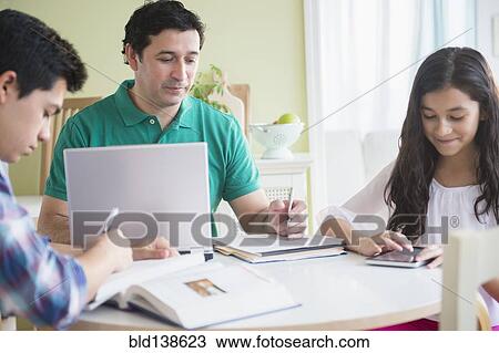 Stock Image - Hispanic family doing homework together at table. Fotosearch