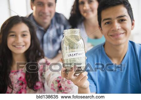 Stock Photography - Hispanic family holding full vacation savings jar. Fotosearch