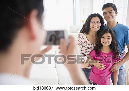Stock Photo - Hispanic family taking cell phone photograph in living room. Fotosearch