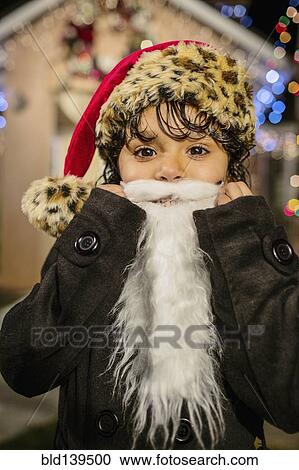 Hispanic girl wearing white beard and Santa hat outside house decorated with string lights View Large Photo Image Stock Image - Hispanic girl wearing white beard and Santa hat outside house decorated with string lights. Fotosearch