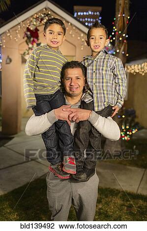 Hispanic man carrying sons on shoulders outside house decorated with string lights View Large Photo Image Stock Image - Hispanic man carrying sons on shoulders outside house decorated with string lights. Fotosearch