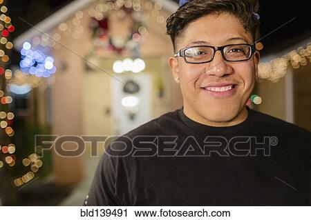 Stock Image - Hispanic man smiling outside house decorated with string lights. Fotosearch