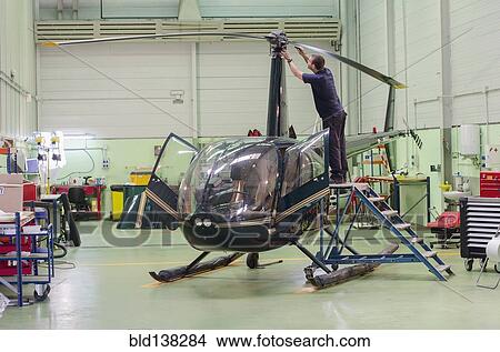 Picture - Hispanic mechanic working on helicopter in hangar. Fotosearch