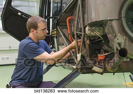 Stock Image - Hispanic mechanic working on helicopter in hangar. Fotosearch