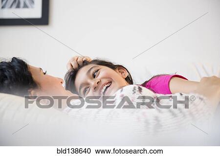 Stock Image - Hispanic mother and daughter relaxing together on bed. Fotosearch