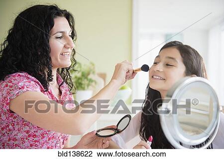 Stock Image - Hispanic mother helping daughter apply makeup. Fotosearch