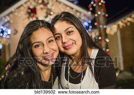 Hispanic sisters smiling outside house decorated with string lights View Large Photo Image Stock Image - Hispanic sisters smiling outside house decorated with string lights. Fotosearch