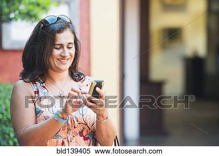 Stock Photography - Hispanic woman using cell phone in city. Fotosearch