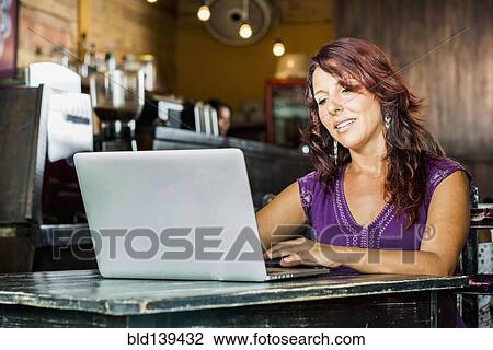 Stock Image - Hispanic woman using laptop in coffee shop. Fotosearch