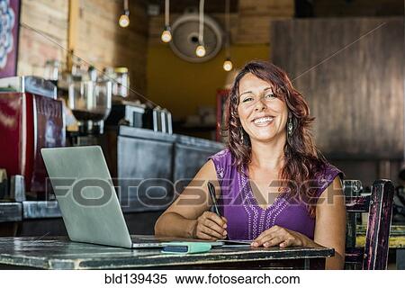 Stock Photography - Hispanic woman using laptop in coffee shop. Fotosearch
