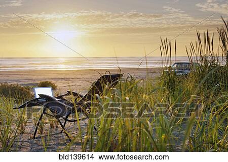 Picture - Laptop on deck chair overlooking sunset on beach. Fotosearch