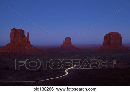 Stock Photograph - Long exposure of car driving past butte rock formations in desert landscape, Monument Valley Tribal Park, Utah, United States. Fotosearch