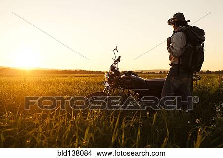 Picture - Mari man standing in field with motorcycle. Fotosearch
