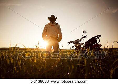 Stock Image - Mari man standing in field with motorcycle. Fotosearch