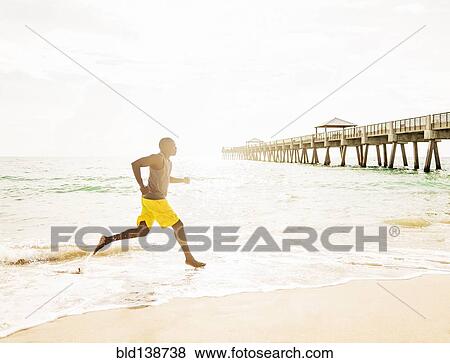 Stock Photo - Mixed race barefoot man running on beach. Fotosearch