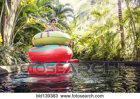 Stock Image - Mixed race boy playing in stacked inner tubes in pool. Fotosearch