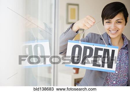 Stock Image - Mixed race businesswoman holding open sign. Fotosearch