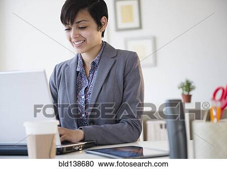 Stock Image - Mixed race businesswoman working on laptop computer at office desk. Fotosearch