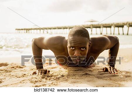 Stock Image - Mixed race man doing push ups on beach. Fotosearch