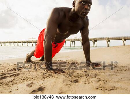 Stock Image - Mixed race man doing push ups on beach. Fotosearch