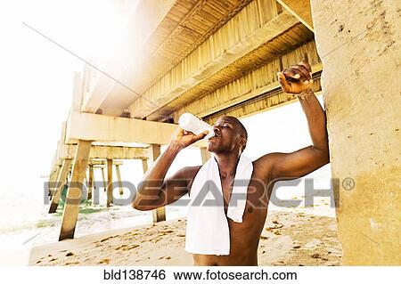 Mixed race man drinking water under pier View Large Photo Image Stock Photograph - Mixed race man drinking water under pier. Fotosearch