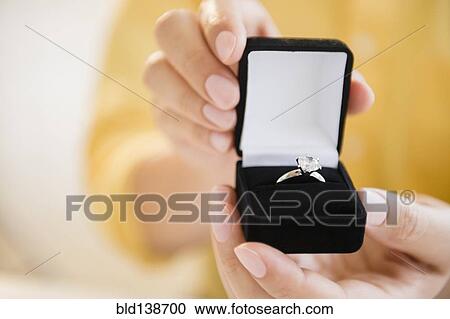 Stock Image - Mixed race man holding engagement ring in box. Fotosearch