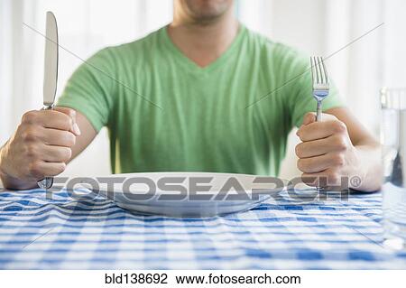 Stock Image - Mixed race man holding fork and knife at table. Fotosearch