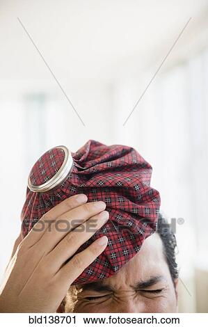 Stock Image - Mixed race man holding ice pack to head. Fotosearch