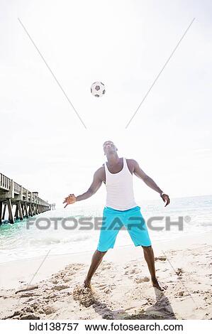 Stock Photo - Mixed race man playing with soccer ball on beach. Fotosearch