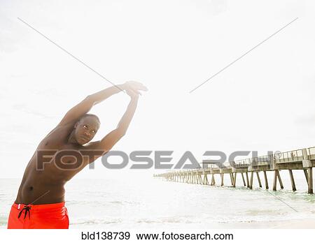 Stock Photo - Mixed race man stretching on beach. Fotosearch