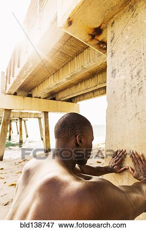 Stock Photo - Mixed race man stretching under pier. Fotosearch