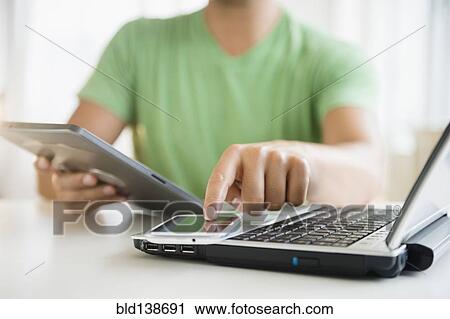 Stock Image - Mixed race man using cell phone, digital tablet and laptop computer. Fotosearch